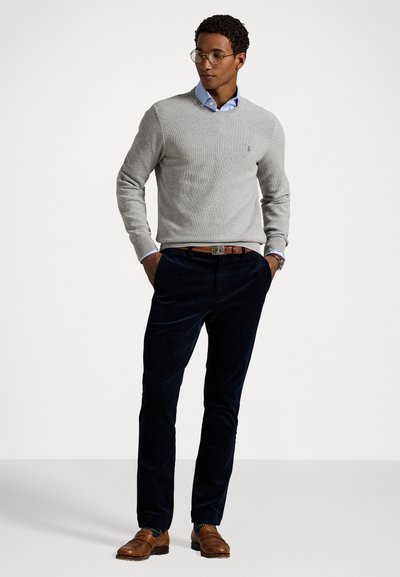 Lys grå strikkegenser, marineblå kordfløyelsbukser, brune skinnsko; lagdelt med en blå skjorte med krage; strukturert og tilpasset design.