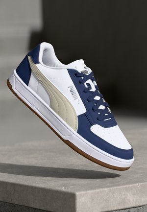 Hvide og navy sneakers har en struktureret panel, polstret tunge og klassisk snørelukning; inkluderer gummisål og Puma-branding accenter.