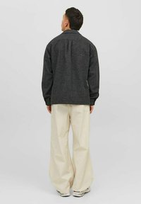 Giacca in misto lana carbone con una vestibilità rilassata, caratterizzata da una piega sul retro e colletto a camicia, abbinata a pantaloni a gamba larga color crema.