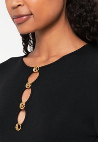 Čierny rebrovaný top s okrúhlym výstrihom a štyrmi zlatými gombíkmi s detailom kľúčovej dierky. Hladká textúra, priliehavý strih.