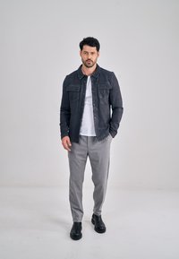 Tmavě modrá džínová bunda se dvěma kapsami na prsou, doplněná šedými kalhotami a černými kotníkovými botami. Pod bundou je jednoduché bílé tričko.