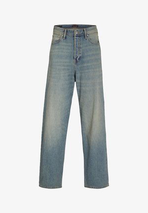Fiú áll előre nézve, sötétszürke "Jack & Jones" pólóban, bő, kék farmerral és barna tornacipővel, egyszerű háttér előtt.