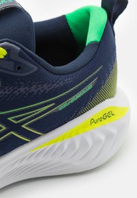 Scarpe da corsa con tomaia in rete blu navy, dettagli verde brillante e suola bianca con un motivo testurizzato. Branding "PureGEL" visibile sul lato.