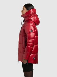 Rode pufferjas met hoge kraag en capuchon, uitgevoerd met een glanzende afwerking, zijzak en logo-accent op de mouw. Ritssluitingen aan de onderkant voor ventilatie.