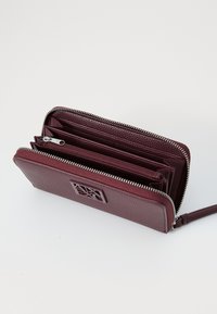 Dark burgundy leather wallet with a textured finish, featuring a zip-around closure, multiple card slots, and a logo accent.