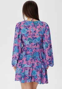 Abito floreale con maniche lunghe nelle tonalità di rosa e blu. Presenta strati a balze, un corpetto aderente e un dettaglio con fiocco sul collo.