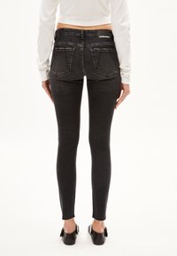 Jeans skinny en denim noir avec une taille mi-haute, dotés de deux poches arrière et d'un ourlet effiloché. Marquage discret sur la ceinture.