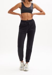 Black sports bra paired with black jogger pants, featuring an elastic waistband, drawstring detail, and contrasting sneakers with light accents.