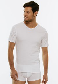 T-shirt bianco in cotone con scollo a V e maniche corte, abbinato a biancheria intima bianca aderente. Texture liscia, design classico e schema di colori semplice.