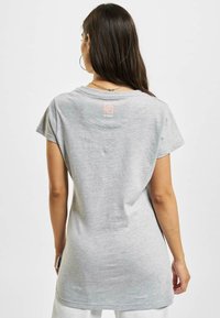 Tricou din bumbac gri, cu mâneci scurte, gât rotund și un logo imprimat în roz pe spate. Textură moale și croială lejeră.