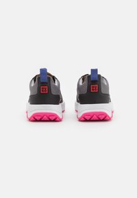 Sneakers neri e grigi con suola rosa. Presentano un linguetta sul tallone di colore blu. Design semplice con tomaia texture e accenti di colore a contrasto.