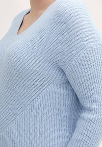 Jasnoniebieski sweter dzianinowy z dekoltem w serek, z teksturowanym wzorem, prążkowanymi detalami i długimi rękawami. Szwy dodają wymiaru.