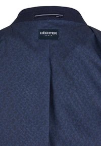 Dunkelblauer Stoff mit einem subtilen geometrischen Muster in hellblau. Enthält ein markiertes Etikett mit der Aufschrift "HÉCHTER PARIS" am Kragen.