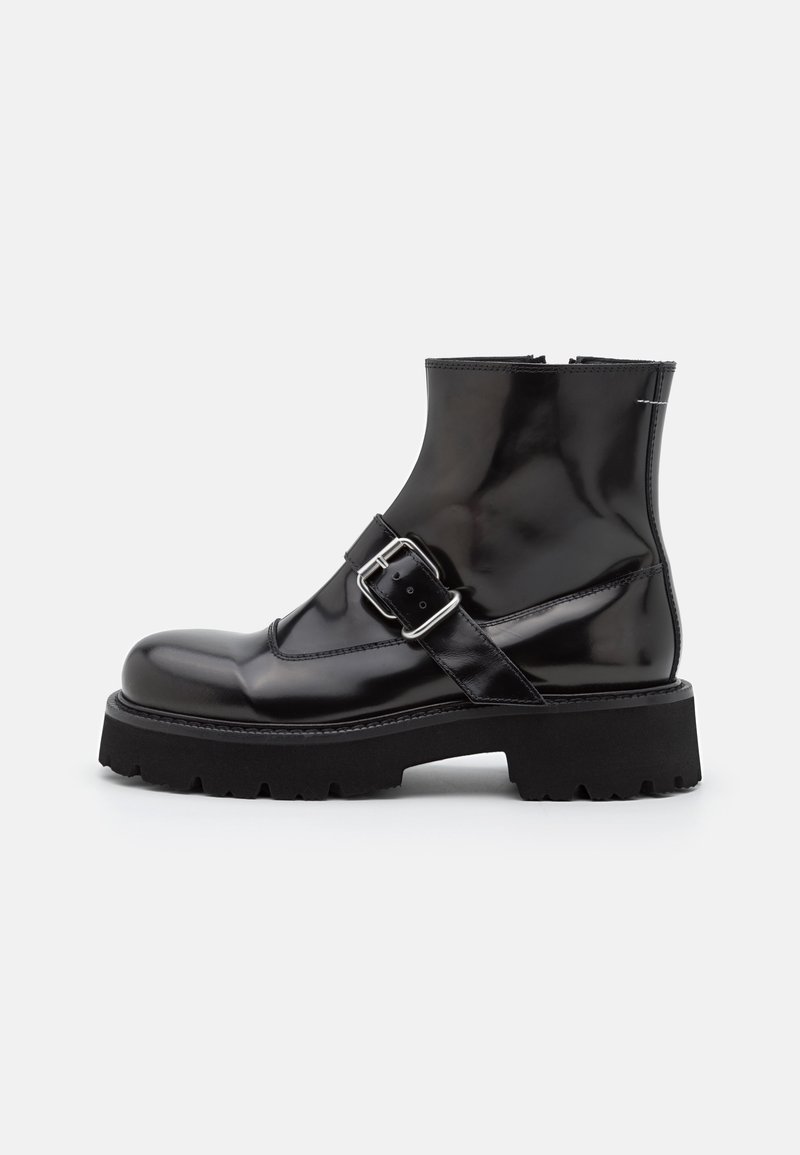 Botas negras hasta el tobillo con un acabado brillante, que cuentan con una correa con hebilla, punta redondeada y una suela gruesa y texturizada para mayor agarre. Textura de cuero suave.