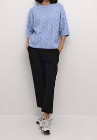 Ljusblå stickad tröja med kabelmönster, sänka axlar, kombinerad med svarta åtsittande byxor och grå sportskor.