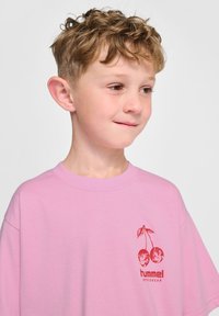Ljusrosa t-shirt i mjuk bomull, med en körsbärsgrafik och texten "hummel SPORTSWEAR" i röd under designen. Rundad halsringning, avslappnad passform.