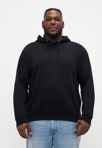 Zwarte katoenen hoodie met een ruime voorzak, capuchon met trekkoord en een ontspannen pasvorm. Heeft lange mouwen en een zachte textuur.