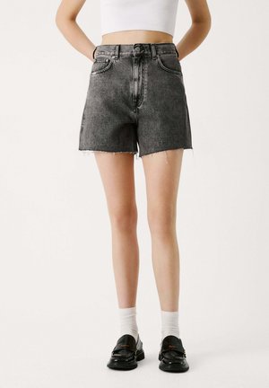 Hoge taille zwarte denim shorts met rafelige zoom, vijfzakken ontwerp en sluiting met een knoop aan de voorkant, gecombineerd met zwarte schoenen en witte sokken.