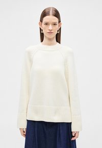 Πλεκτό πουλόβερ σε κρεμ απόχρωση με ριμπ τελείωμα στη μέση και στα μανίκια, κλασικό στρογγυλό λαιμόκομμα και ραγκλάν μανίκια για άνετη εφαρμογή.