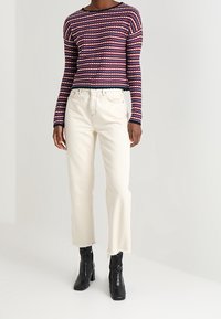 Gebreide trui met rode, marineblauwe en witte strepen; cropped ontwerp. Witte recht gesneden jeans met rafelige zoom. Zwarte enkellaarzen.