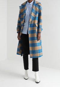 Cappotto lungo a quadri marrone e blu, realizzato in tessuto testurizzato, con chiusura doppiopetto, ampi revers e tasche laterali.