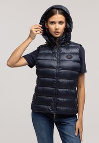Granatowa puchowa kamizelka z kapturem, z zamkiem błyskawicznym z przodu, dwoma bocznymi kieszeniami oraz logo na klatce piersiowej. Gładka tekstura i pikowana konstrukcja.