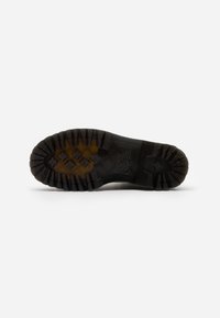 Czarna gumowa podeszwa butów z głębokim bieżnikiem, z heksagonalnymi i prostokątnymi wzorami oraz widocznym wytłoczonym logo marki z boku.