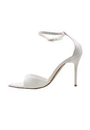 Sandalo bianco con tacco alto, punta appuntita, cinturino alla caviglia e tacco a spillo su sfondo bianco.