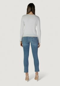 Maglietta bianca a maniche lunghe con texture a coste, abbinata a jeans skinny azzurri chiari con tasche posteriori. La modella indossa tacchi trasparenti.