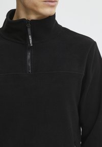 Sort fleece pullover med høj krave og zippet åbning. Fås med en glat tekstur, syninger på tværs af brystet og et logo på zippen.
