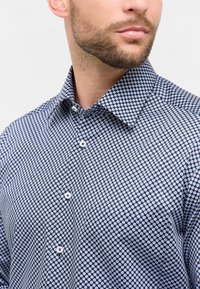 Camicia a bottoni patterned in blu navy e bianco, con un design geometrico, colletto aperto e bottoni bianchi con una finitura in tessuto testurizzato.