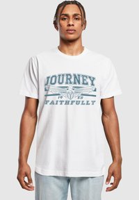 Baltas medvilnės marškinėlis su mėlyna grafika "JOURNEY 1983 FAITHFULLY" ir sparnuotu dizainu priekyje. Trumpomis rankovėmis, laisvesnio silueto.