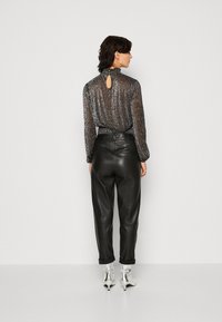 Blouse noire transparente avec une finition texturée, dotée d'un dos clé et d'un col froncé, assortie de pantalons en cuir noir taille haute et de bottes argentées.