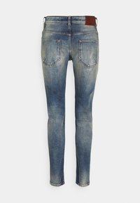 Slim-fit niebieskie dżinsy o wyblakłym wyglądzie, pięć kieszeni i brązowa skórzana naszywka na pasie. Prosta nogawka z minimalnym przeszyciem.