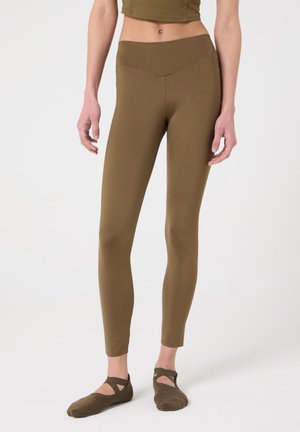 Leggings ajustados de color verde oliva combinados con una camiseta a juego y zapatillas estilo ballet sobre un fondo neutro.