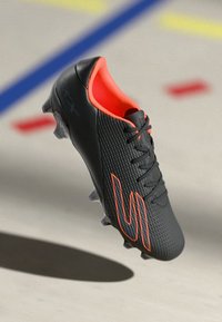 Black soccer cleat with textured surface, orange accents, and visible lacing, designed for performance with a sleek, aerodynamic shape.