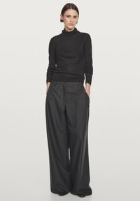 Maglione a collo alto nero in filato fine abbinato a pantaloni ampi grigio antracite con righe. Vestibilità sartoriale con tasche e dettagli sottili in vita.