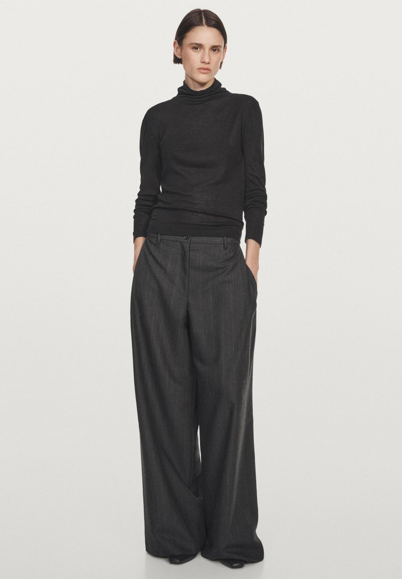 Maglione a collo alto nero in filato fine abbinato a pantaloni ampi grigio antracite con righe. Vestibilità sartoriale con tasche e dettagli sottili in vita.