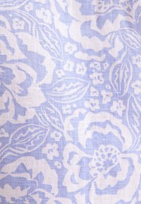 Tissu bleu clair avec un motif floral blanc comprenant de grandes fleurs, des feuilles et de petites fleurs éparses dans une texture tissée.