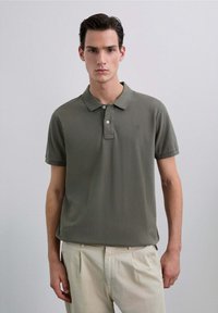 Polo de color verde oliva en mezcla de algodón, con cuello clásico, dos botones, mangas cortas y un discreto detalle de logotipo bordado.