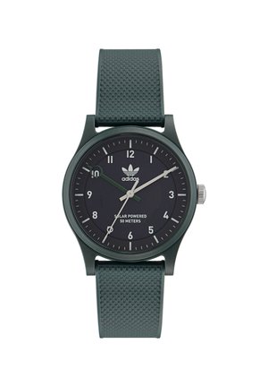 Montre solaire verte avec un bracelet texturé, un cadran noir, des index horaires blancs et verts, et un accent en acier inoxydable sur la couronne.