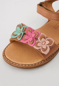 Bruine leren sandaal met een gestructureerde voetbed, versierd met gelaagde stoffen bloemen in roze, teal en bruin over de band.