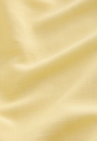 Tissu jaune doux avec une texture en grille subtile et des plis délicats créant des variations de lumière et d'ombre.