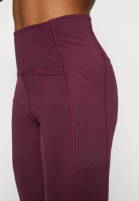 Magas derekú leggings sötét burgundi színben, rugalmas anyagból készült. Panelvarrással és sima tapintással rendelkezik.