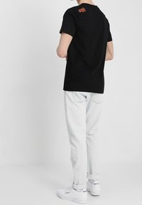 Černé bavlněné tričko s kulatým výstřihem a krátkými rukávy, s červeným vyraženým logem na zadní straně, spárované se světlými denimovými džínami.