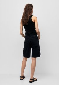 Top de tirantes negro, pantalones cortos cargo oscuros con bolsillos laterales, dobladillo deshilachado y sandalias planas. Tejido suave con un corte casual y un diseño sencillo.