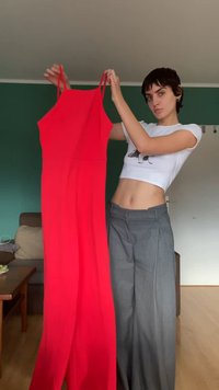Czerwona kombinezon bez rękawów z dopasowanym korpusem, szerokimi, swobodnie opadającymi nogawkami oraz cienkimi ramiączkami, zaprezentowany na zielonym tle.
