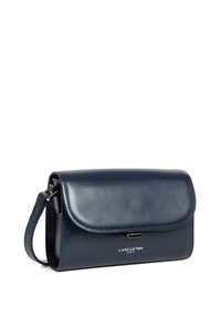 Pochette en cuir marine avec rabat repliable, bandoulière amovible et quincaillerie en argent. Présente le logo de la marque en relief à l'avant.