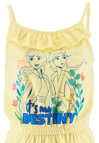 Salopette di tessuto giallo con spalline arricciate, caratterizzata da una grafica blu di due personaggi circondati da fiori, e testo blu che recita "è il mio DESTINO."