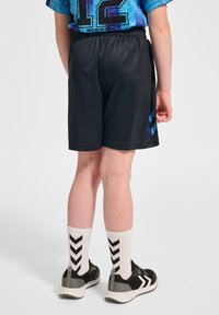 Svarta atletiska shorts med elastisk midja, kombinerade med vita strumpor med svarta chevronmönster och svarta sneakers.